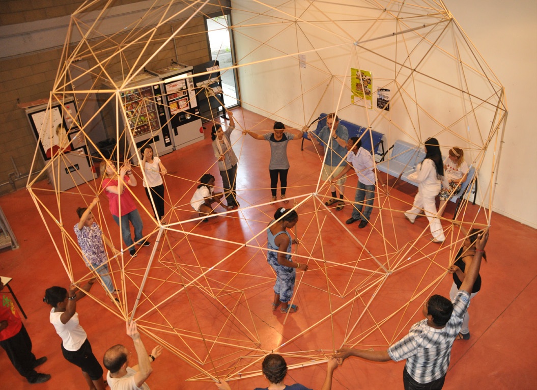 Des enfants construisent un polydre gant avec des tiges de bois dans un gymnase.