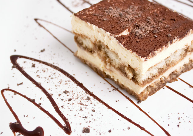 part de tiramisu rectangulaire avec une traine zigzagante de chocolat sur l'assiette